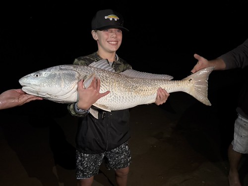 Young man holding a large reddish fish at night